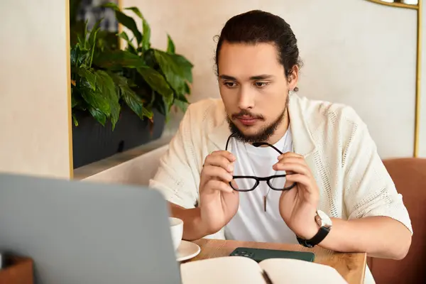 A young man with a beard focuses on his laptop while sipping coffee in a cafe. — Stock Photo
