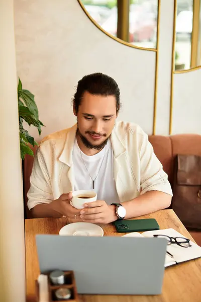Bearded man works on his laptop in a cafe, savoring a warm beverage and sunlight. — Stock Photo
