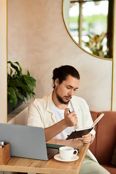 Young man with a beard is focused on writing notes while sipping coffee in a cozy cafe. — Stock Photo