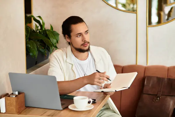 A bearded young man works remotely at a cafe, jotting notes while sipping coffee. — Stock Photo