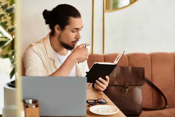 A bearded young man sips coffee and takes notes in his journal at a cozy cafe. — Stock Photo