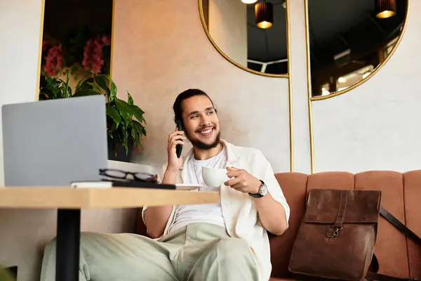 A young man with a beard smiles while working remotely in a cafe, enjoying coffee and conversation. — Stock Photo