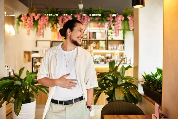 Young man with a beard smiles in a lively cafe setting filled with greenery. — Stock Photo