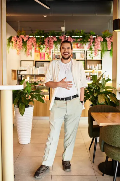 A young man with a beard standing cheerfully in a lively cafe filled with greenery. — Stock Photo