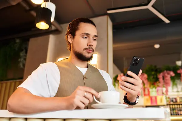 Freelancer dedicado al trabajo remoto, bebiendo café y usando su teléfono inteligente en un animado entorno de cafetería. - foto de stock