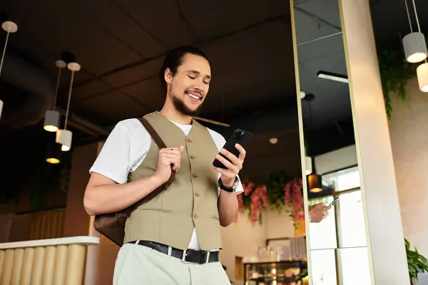 Joven con barba comprueba su teléfono en un animado café durante el verano. — Stock Photo