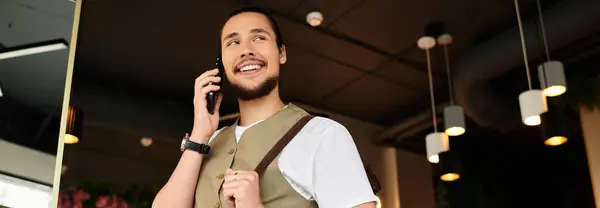 A young man with a beard smiling during a phone call at a cafe, banner — Stock Photo