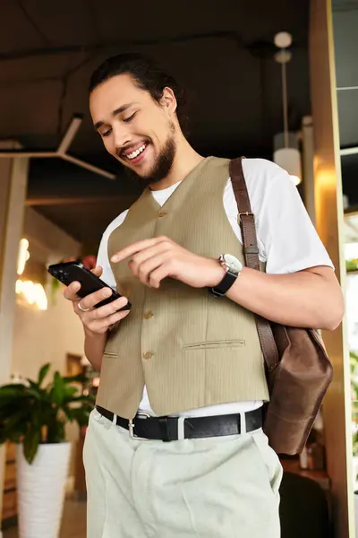 Joven con barba se dedica a un trabajo remoto, sonriendo mientras usa su teléfono inteligente en un café. - foto de stock