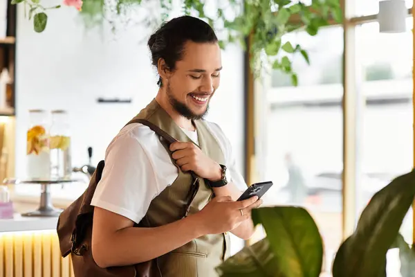 Freelancer se involucra con su smartphone mientras se relaja en un café lleno de vegetación. — Stock Photo