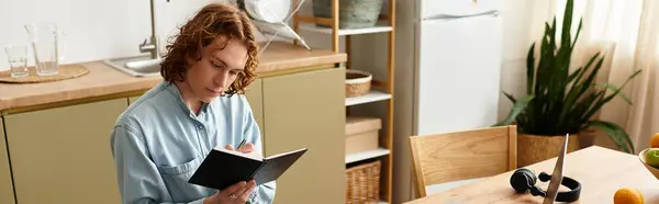Красивый молодой человек сидит за деревянным столом, пишет в блокноте с фокусом, расслабляется дома. — стоковое фото