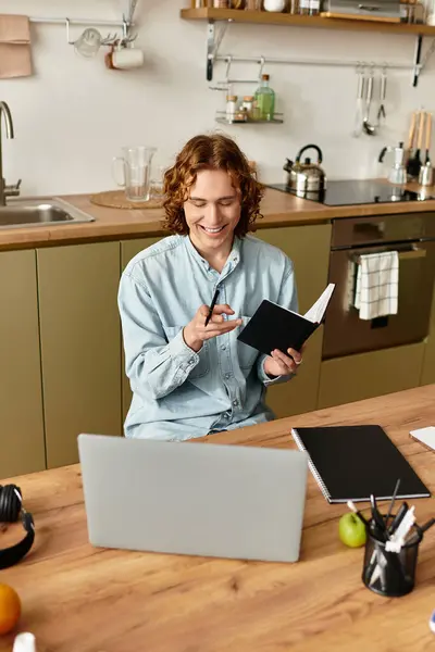 A young man sits comfortably in his kitchen, writing notes and enjoying his creative process. — Stock Photo