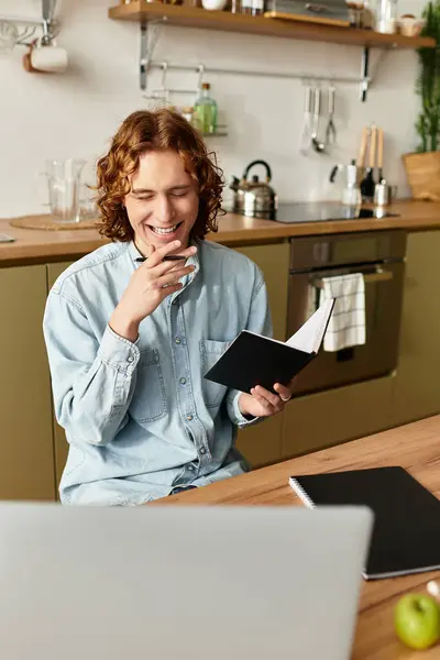 Bel giovanotto a casa sorride bevendo caffè e annotando nel suo taccuino in una giornata di sole. — Foto stock