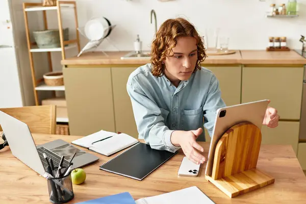 A young man at a cozy kitchen table, immersed in creativity on his tablet. — Stock Photo