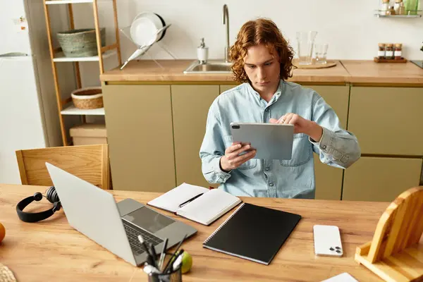 Handsome young man is diligently working on a tablet at his cozy home workspace, immersed in tasks. — Stock Photo