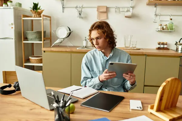 Handsome young man focuses on his tablet while seated at a wooden table in a cozy home setting. — Stock Photo