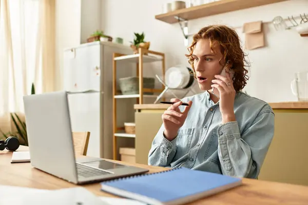 A young man with curly hair chats happily on the phone in his cozy home office. — Stock Photo