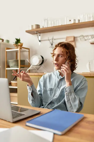 A young man in casual clothes talks on the phone at a cozy desk. — Stock Photo