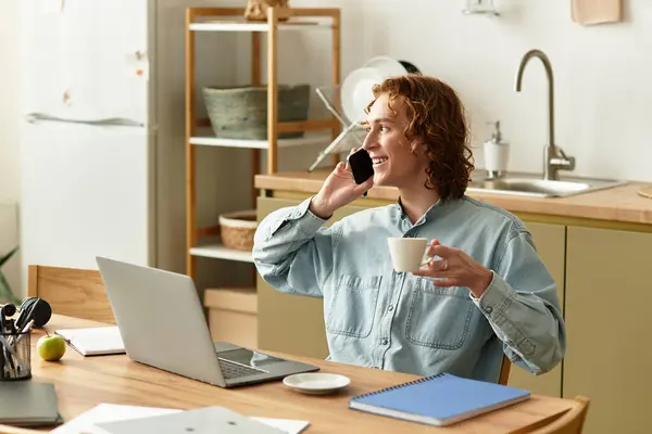 Young man sits comfortably at a home workspace, talking on the phone and enjoying his drink. — Stock Photo