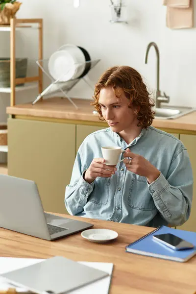 Young man relaxed at home, savoring coffee and focused on his laptop, creating a warm atmosphere. — стоковое фото