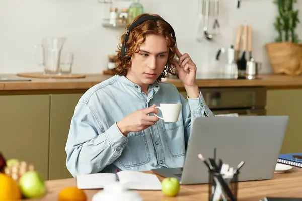 Handsome man with curly hair focuses on his laptop while sipping a warm beverage at home. — Stock Photo