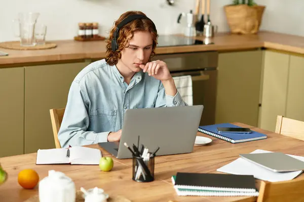 Concentrated young man engages in remote work at his kitchen table surrounded by notes. — Stock Photo