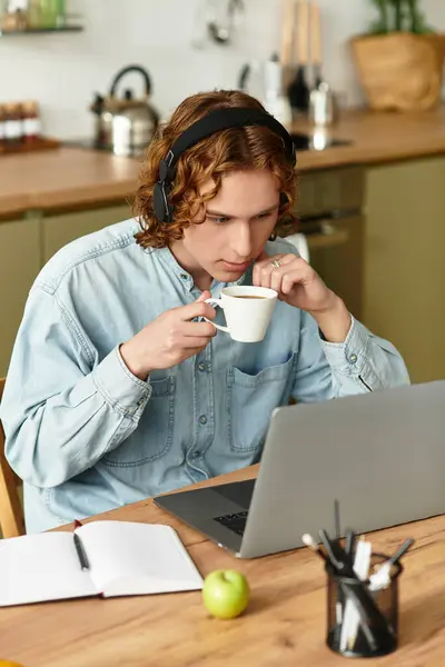 Handsome young man sits at his desk, sipping coffee while focusing on his laptop screen. — Stock Photo