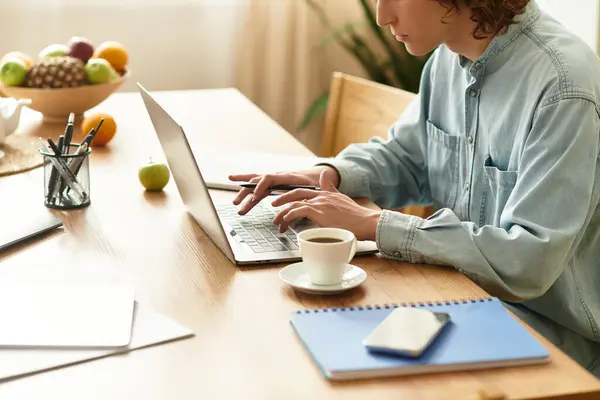 Focused young man sits at a wooden table, typing on his laptop and sipping coffee. — Stock Photo