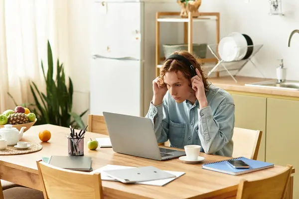 A young man sits at a dining table, engaged with his laptop and headphones, deep in concentration. — Stock Photo