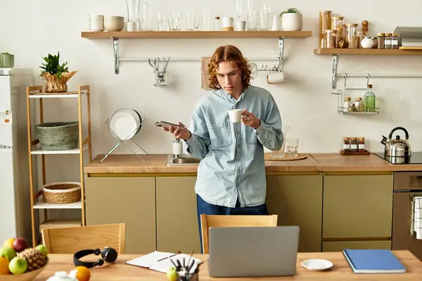 A stylish young man sips coffee in a modern kitchen, looking thoughtfully at his smartphone. — Stock Photo