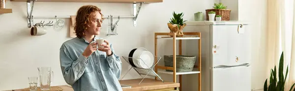 A young, handsome man relaxes in a cozy kitchen while savoring a delightful drink. — Stock Photo