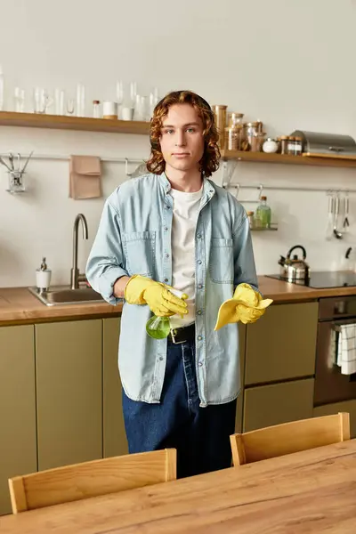 A young man wearing a casual outfit and gloves cleans the kitchen, smiling cheerfully. — Stock Photo