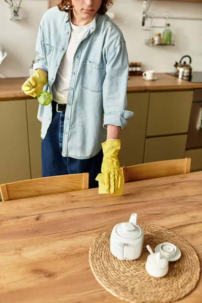 A handsome young man tidies up the wooden dining table, preparing for a meal in his warm kitchen. — Stock Photo