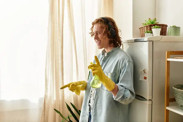Happy young man laughs while cleaning his kitchen, dressed in casual attire and gloves. — Stock Photo