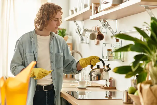 In a chic kitchen, a young man in gloves enjoys making tea at home. — Stock Photo