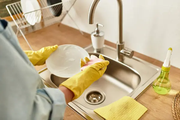 Handsome young man wearing gloves washes dishes in a welcoming kitchen setting. — Stock Photo