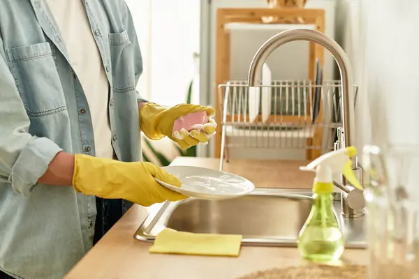 A young man with a charming smile washes dishes at home, surrounded by a sunlit kitchen. — Stock Photo