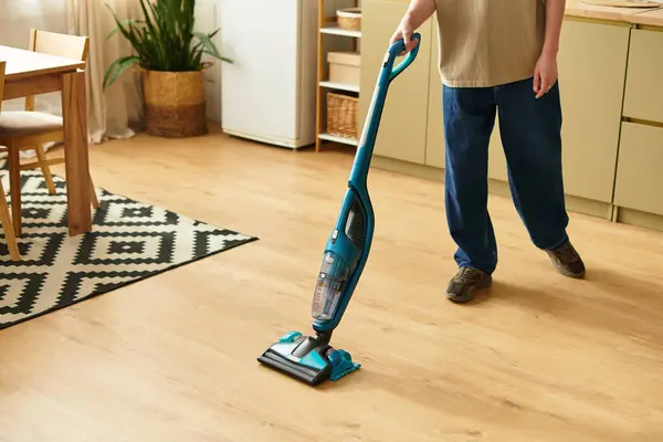 Joven hombre ordena su elegante casa mientras usa una aspiradora azul en el suelo. - foto de stock