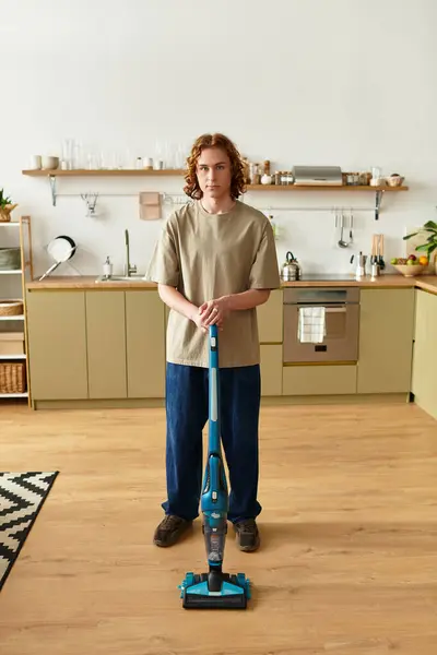 Joven se para con confianza en casa, utilizando un vacío para ordenar su amplia área de cocina. - foto de stock