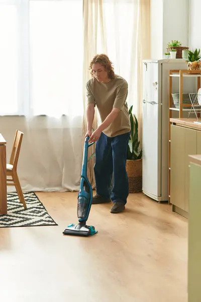 Handsome young man tidies up his living area, using a vacuum cleaner in the warm sunlight. — Stock Photo