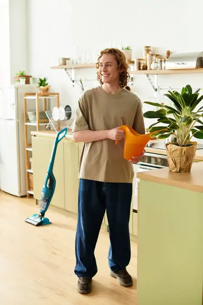 Smiling young man holding a watering can, tending to plants in a modern kitchen filled with warmth — Stock Photo