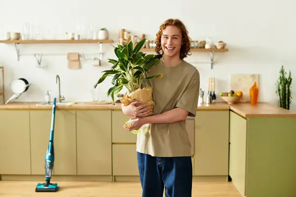 A joyful young man in a stylish kitchen proudly holds a potted plant. — Stock Photo