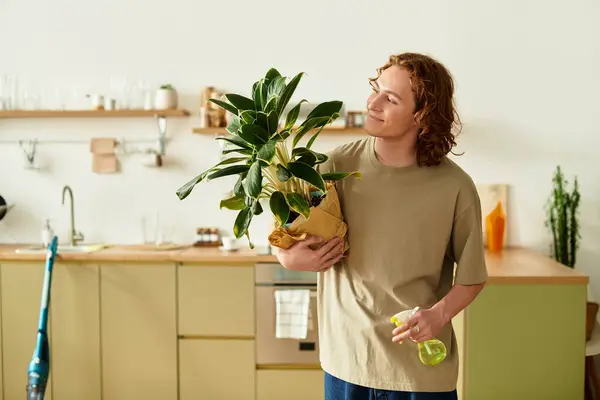 Joven con el pelo rizado disfruta de la crianza de una planta de interior mientras está rodeado por una cocina elegante. - foto de stock