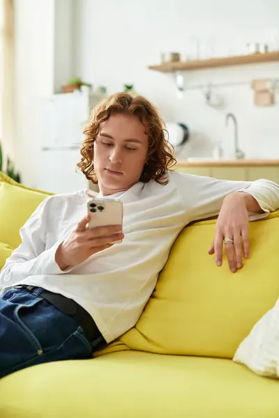 A young man lounges on a yellow couch, absorbed in his smartphone amidst a cozy home atmosphere. — Stock Photo