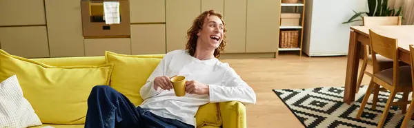 Bright and cheerful atmosphere as a young man lounges on a yellow sofa, sipping from his cup. — Stock Photo