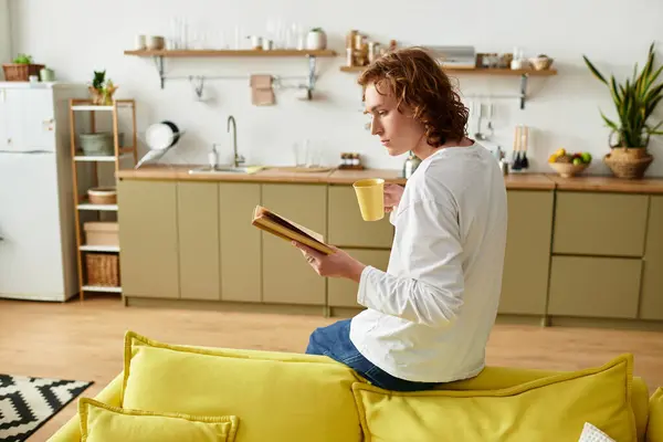 A young man enjoys a quiet afternoon at home, sipping tea while engrossed in a book. — Stock Photo