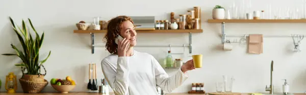 Handsome young man at home engages in a lively phone call, savoring a warm beverage. — Stock Photo