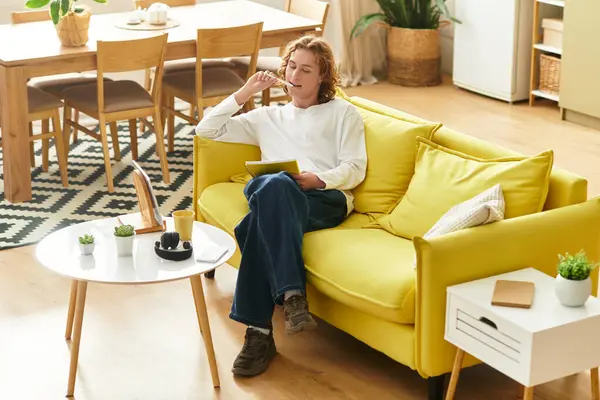 Relaxing on a vibrant couch, a young man enjoys his drink while contemplating his thoughts. — Stock Photo
