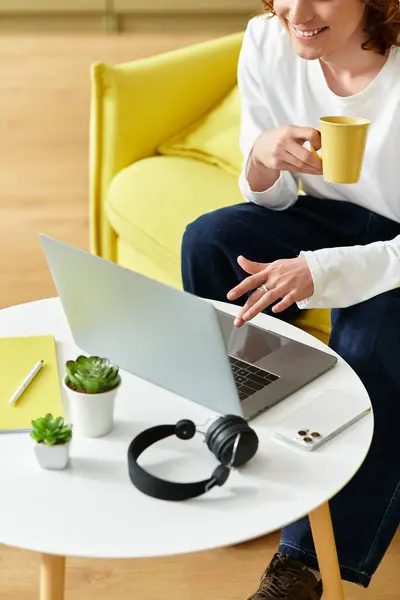 Handsome young man sips coffee and interacts with his laptop in a vibrant home workspace. — Stock Photo