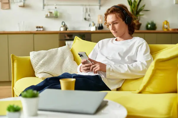 A handsome young man relaxes on a yellow couch, focused on his smartphone at home. — Stock Photo