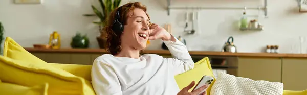 Young man listens to music with headphones, smiling joyfully while lounging at home. — Stock Photo